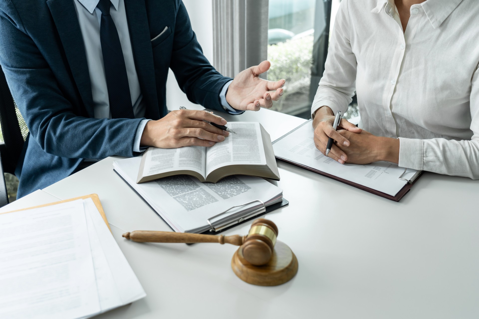 Male lawyer is pointing on legal document to explaining about consultation terms and condition to businesswoman before signing on contract at law firm